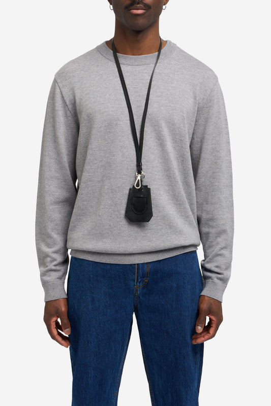 Men's accessories, black vegetable-tanned leather key chain with Bluetooth tracker compartment, worn over a grey knit sweater.