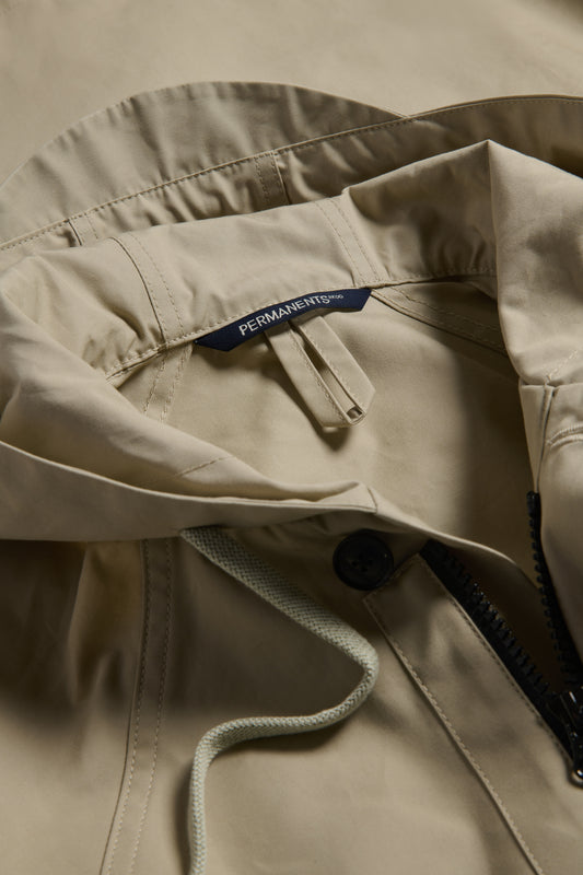 Men's outerwear parka, organic cotton, stone, featuring an adjustable hood, drawstring, and black zipper.