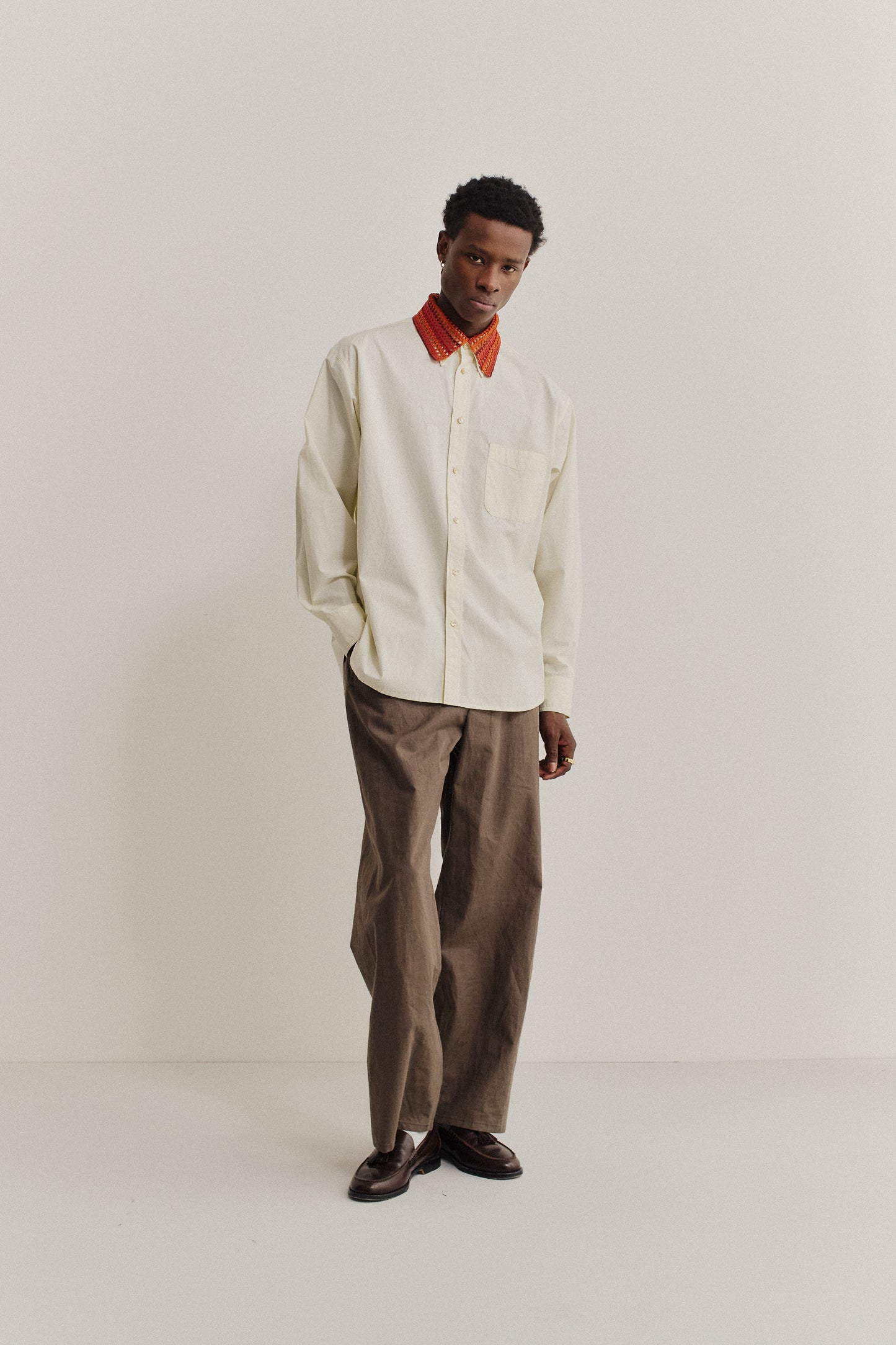 Men's accessories, hand-crocheted Kikoy Collar in red and orange merino wool, worn over a cream linen-cotton shirt.