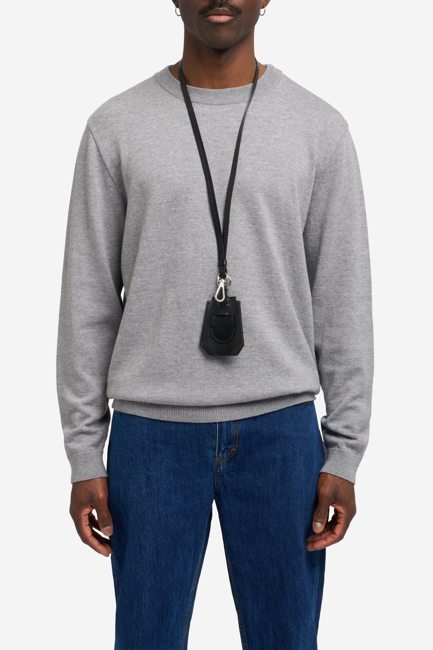 Men's accessories, black vegetable-tanned leather key chain with Bluetooth tracker compartment, worn over a grey knit sweater.