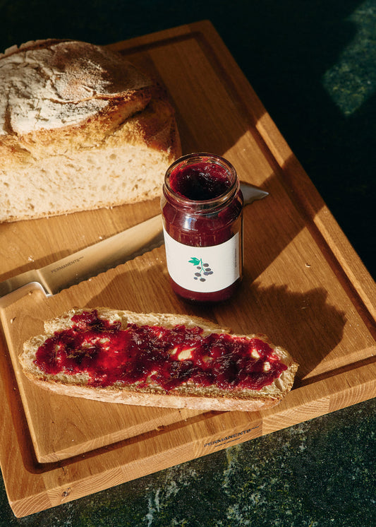 Oak wood chopping board with juice groove, featuring a jar of berry jam and a slice of bread with jam.