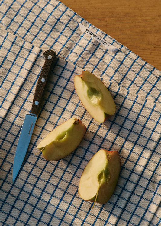 Office knife, 10cm steel blade with dark bog oak handle, next to apple slices on a blue and white checkered cloth.