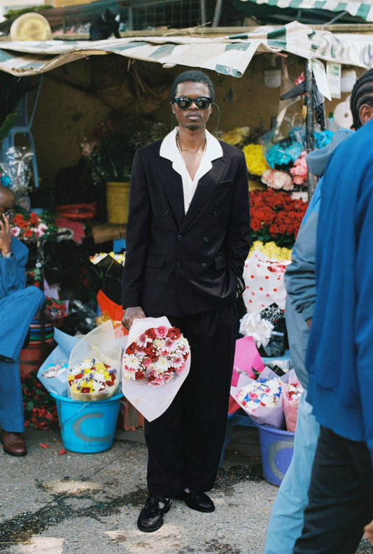 Men's tailoring, double-breasted peak blazer in checkered black virgin wool, relaxed fit, holding flowers.