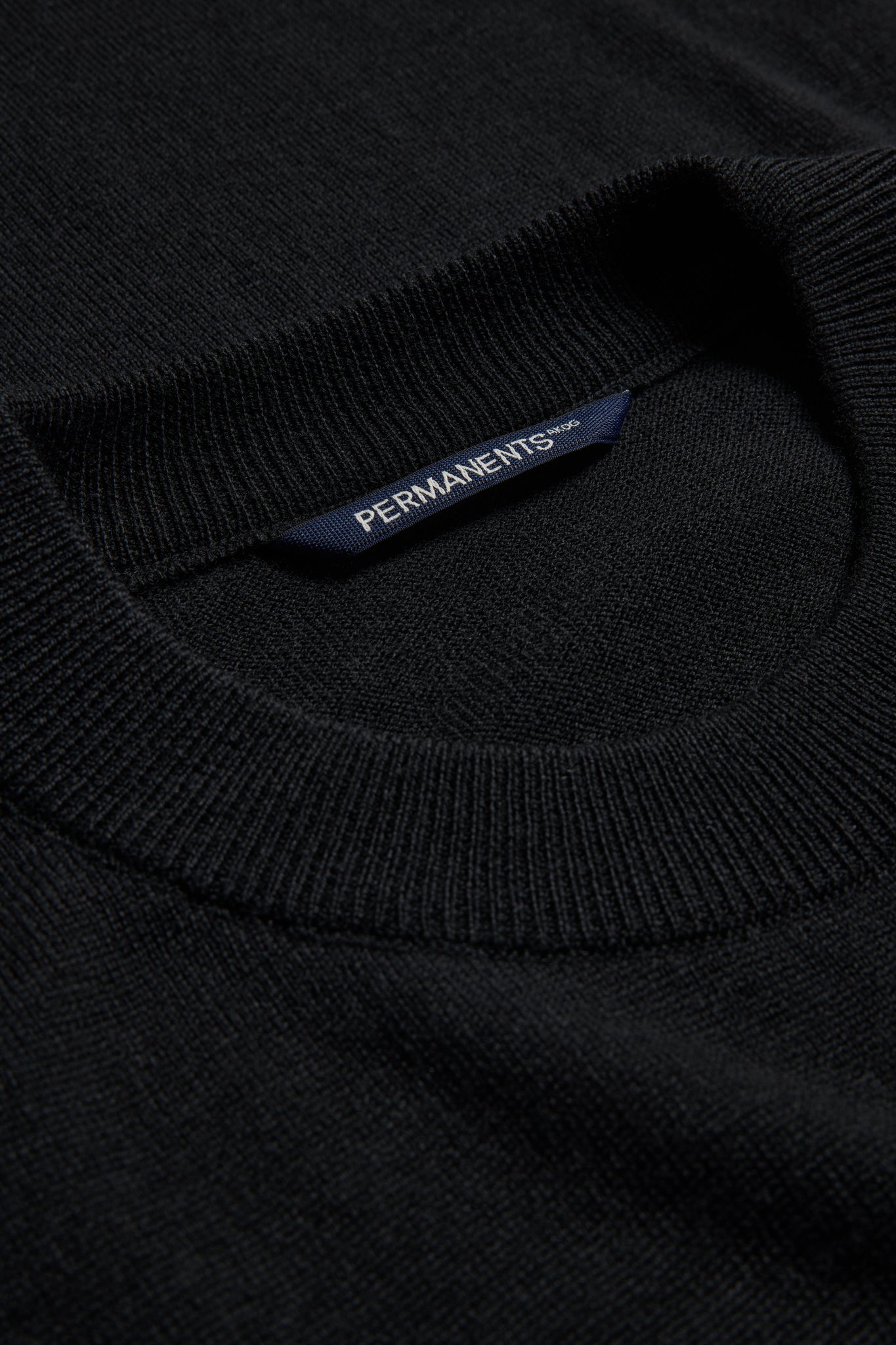 Unisex knit crewneck, black mulesing-free merino wool, with ribbed neck and PERMANENTS® label.