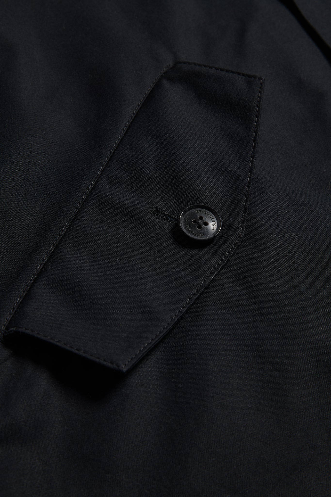 Unisex outerwear parka, black organic cotton EtaProof fabric, close-up of flap pocket with button.