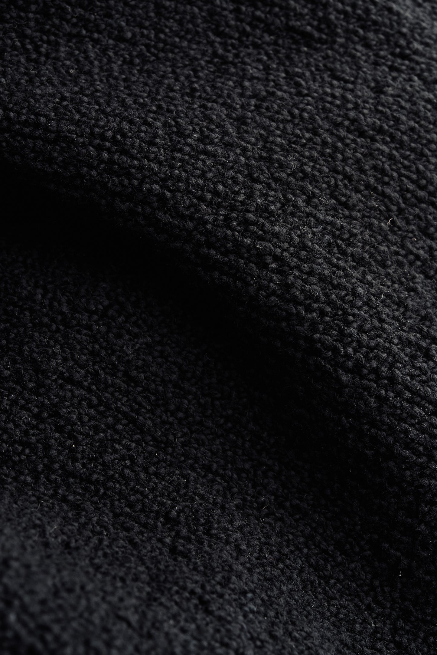 Men's knit short-sleeved polo, black 100% organic cotton bouclé, close-up of tactile texture.