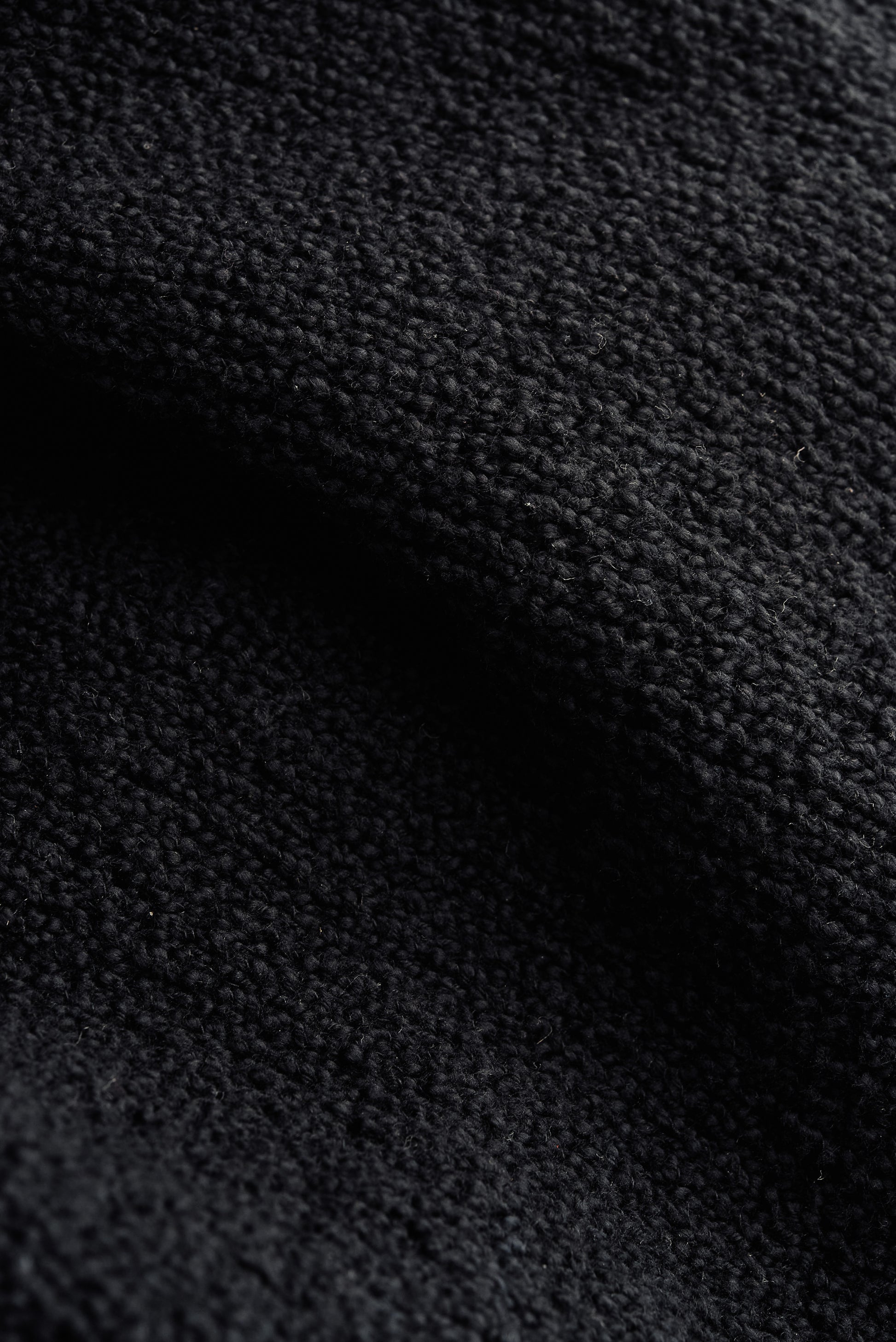 Men's knit short-sleeved polo, black 100% organic cotton bouclé, close-up of tactile texture.