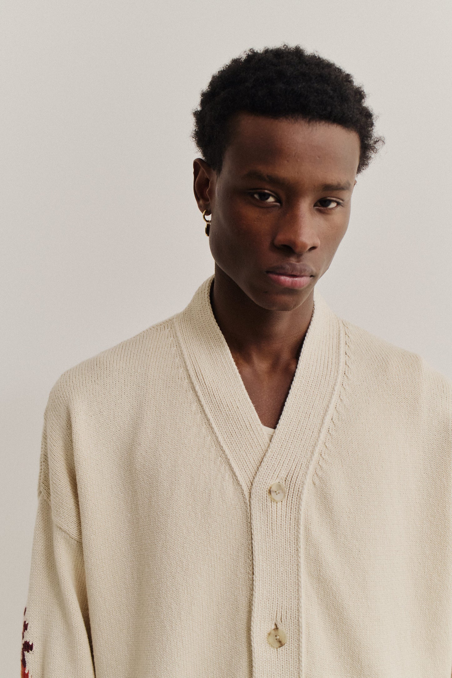 Men's knit cardigan, cotton-cashmere blend, cream, with deep V-neck, ribbed cuffs, and embroidered elbow details.