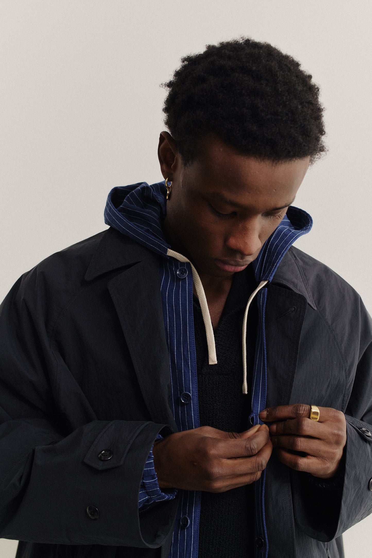 Men's outerwear, oversized navy recycled nylon-cotton blend Serrara Mac jacket with reverse collar, worn over a striped hoodie.