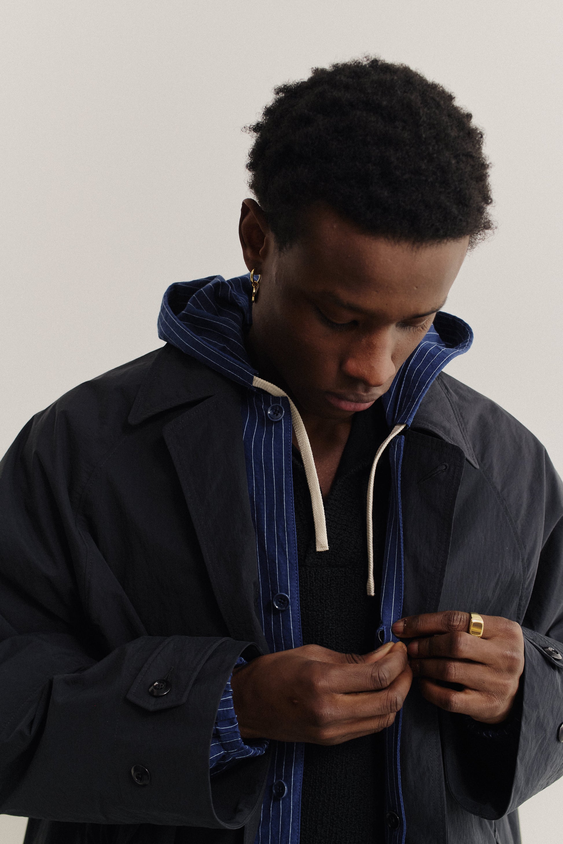 Men's outerwear, oversized navy recycled nylon-cotton blend Serrara Mac jacket with reverse collar, worn over a striped hoodie.