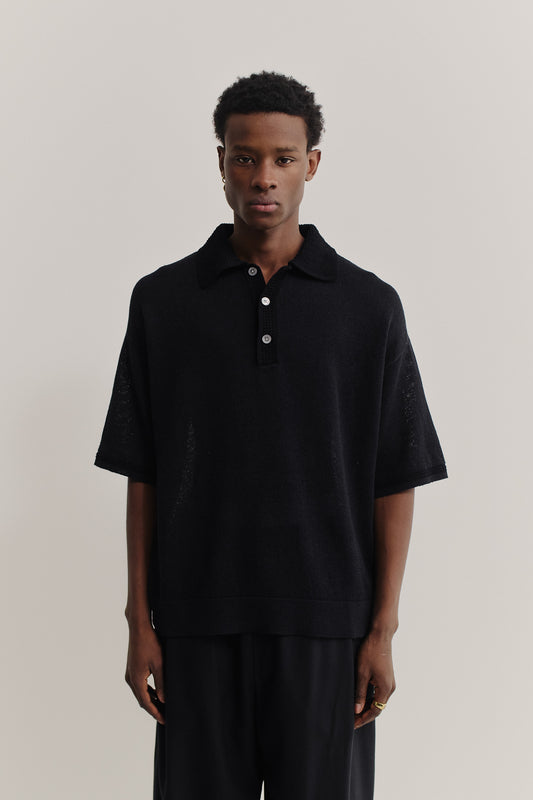Men's knit short-sleeved polo, black linen-organic cotton blend, oversized fit, spread collar, white buttons.