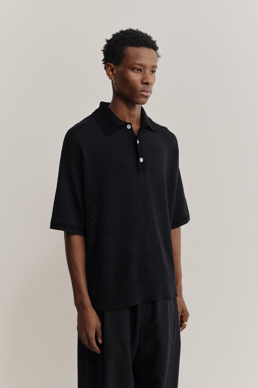 Men's knit short-sleeved polo, black linen-organic cotton blend, oversized fit, spread collar, white buttons.