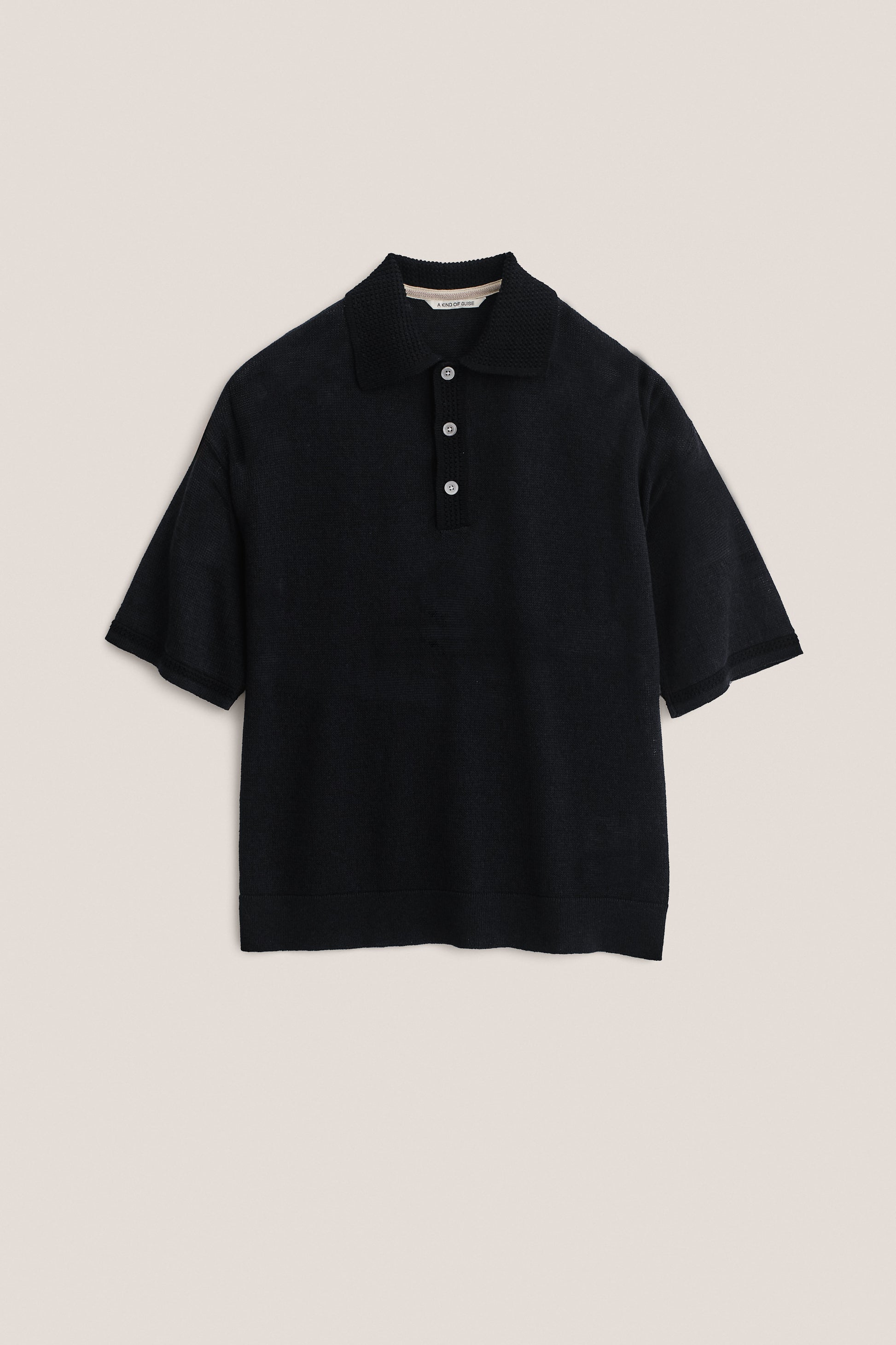 Men's knit short-sleeved polo, black linen-organic cotton blend, with spread collar and three white buttons.