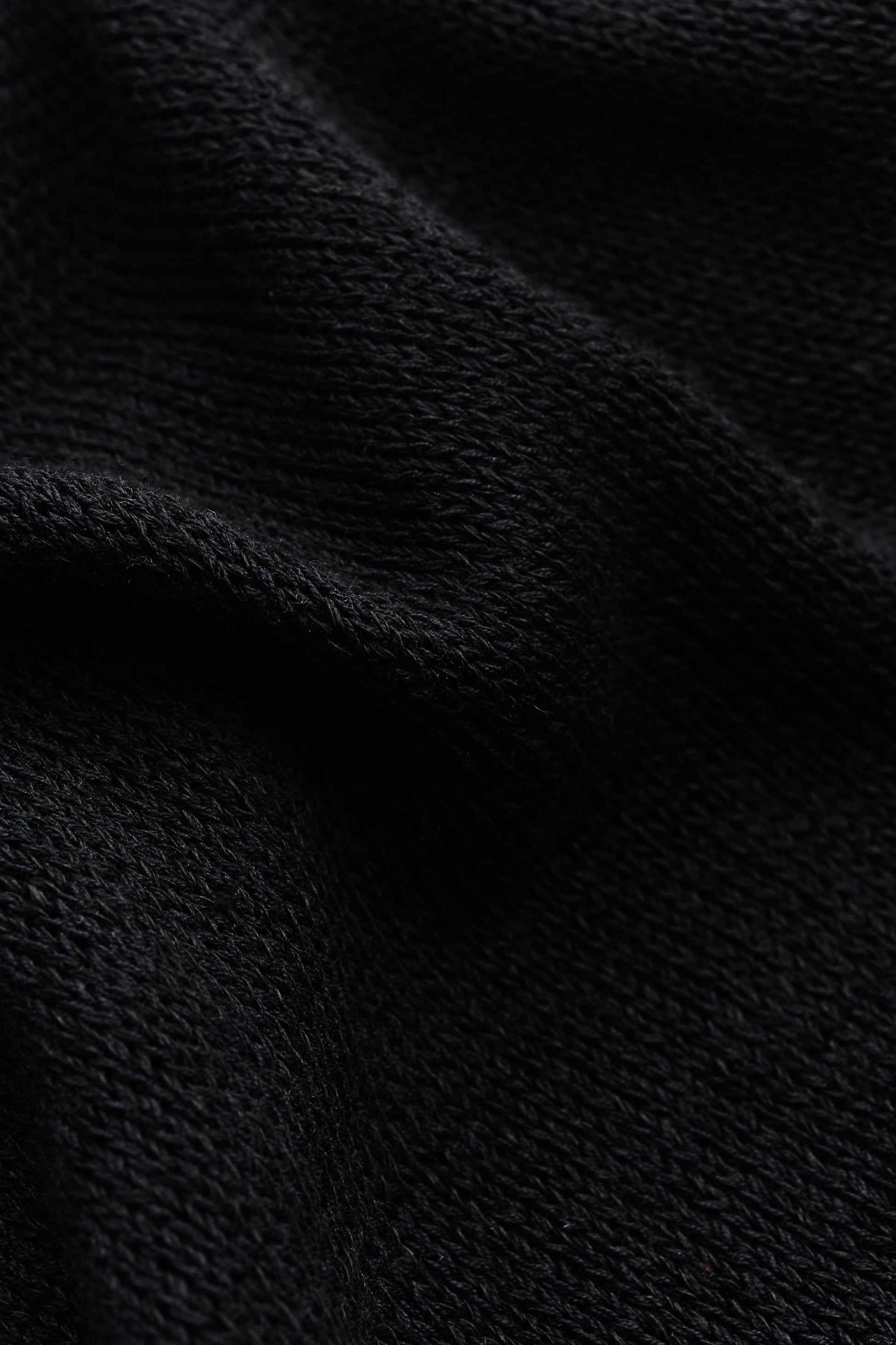 Men's knit short-sleeved polo, black linen-organic cotton blend, close-up of light knit texture.