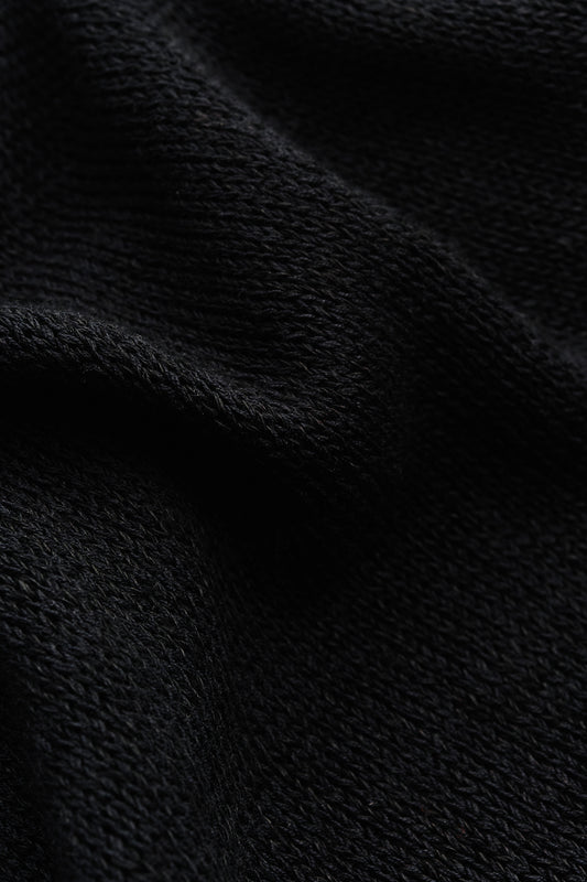 Men's knit short-sleeved polo, black linen-organic cotton blend, close-up of light knit texture.