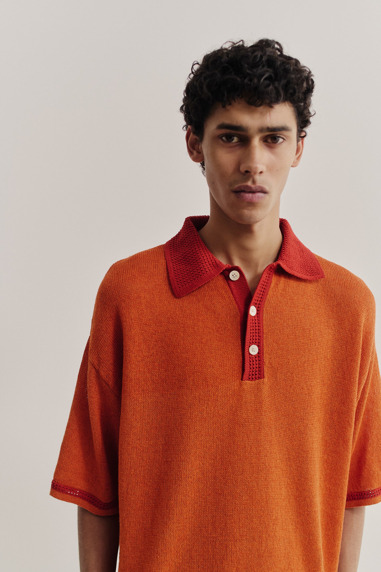 Men's knit short-sleeved polo, linen-organic cotton blend, orange with red contrast collar and sleeve stripe.