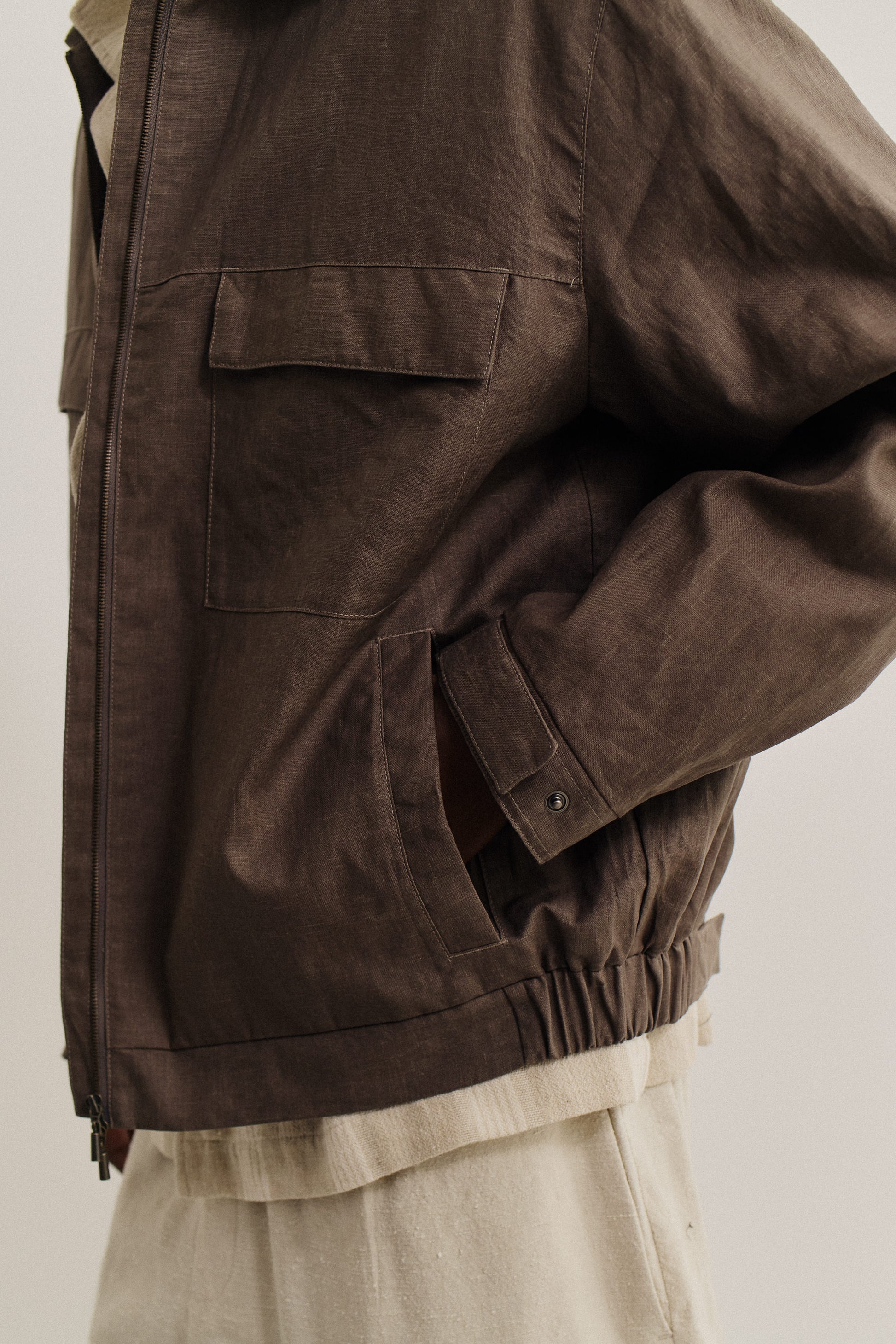 Men's outerwear jacket, 100% linen, natural brown, with flap chest pockets, welt pockets, elasticated waist, and front zip.