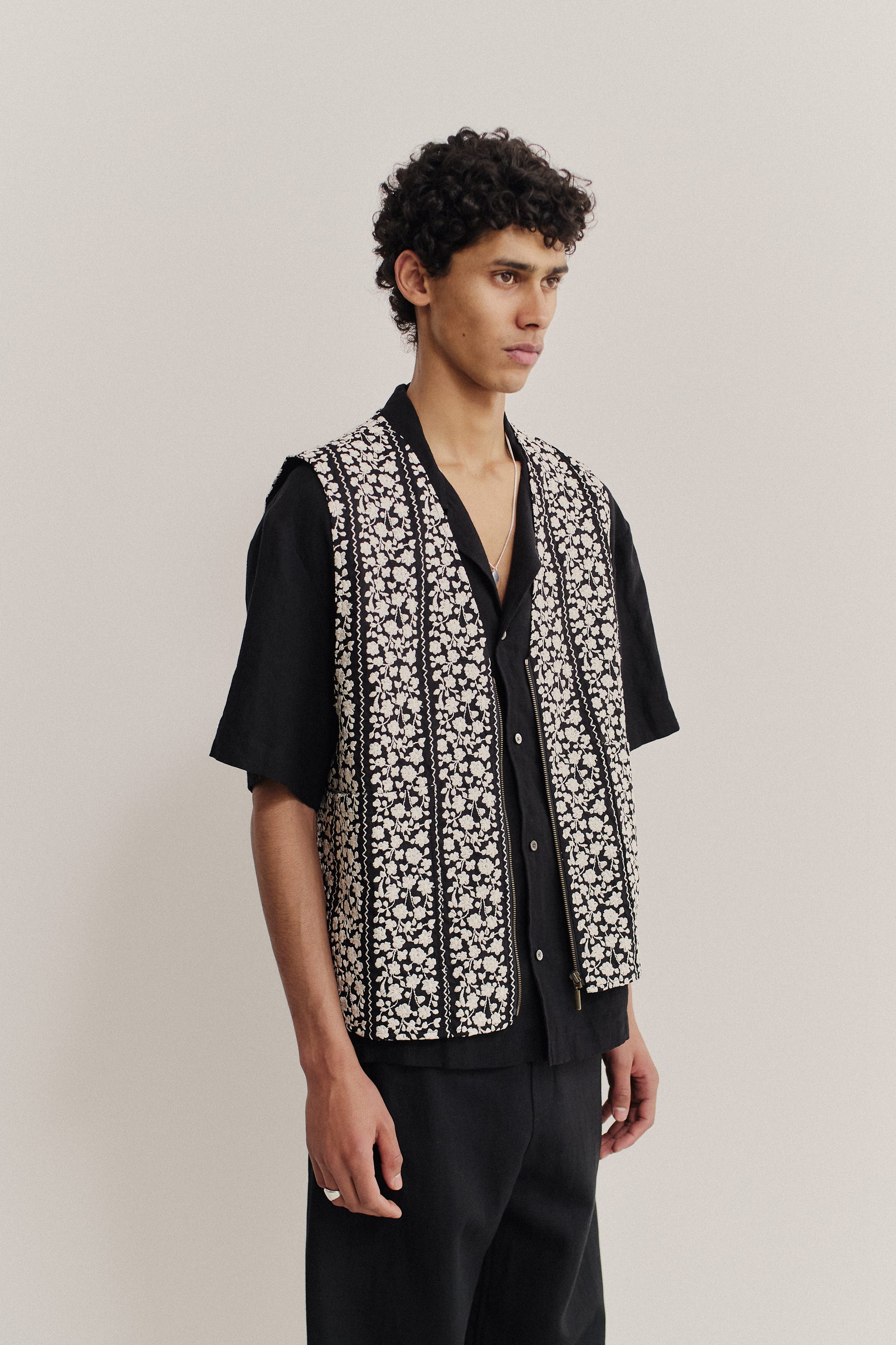 Men's outerwear vest, black cotton with white embroidered floral blocks, metal zipper, oversized fit.