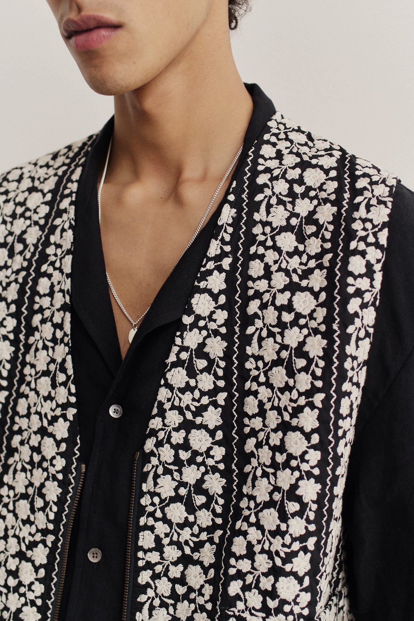 Men's outerwear vest, black cotton with white embroidered floral blocks and a metal zipper.