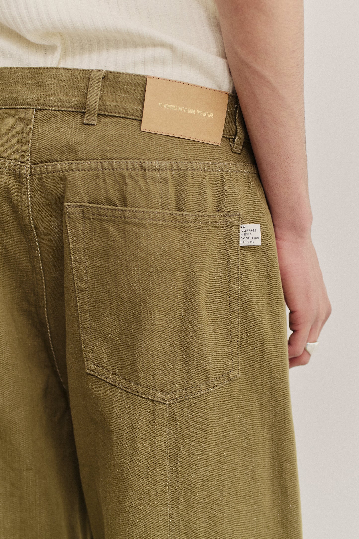 Men's long-pants, cotton selvedge denim, olive green, with a leather brand patch and back pocket detail.