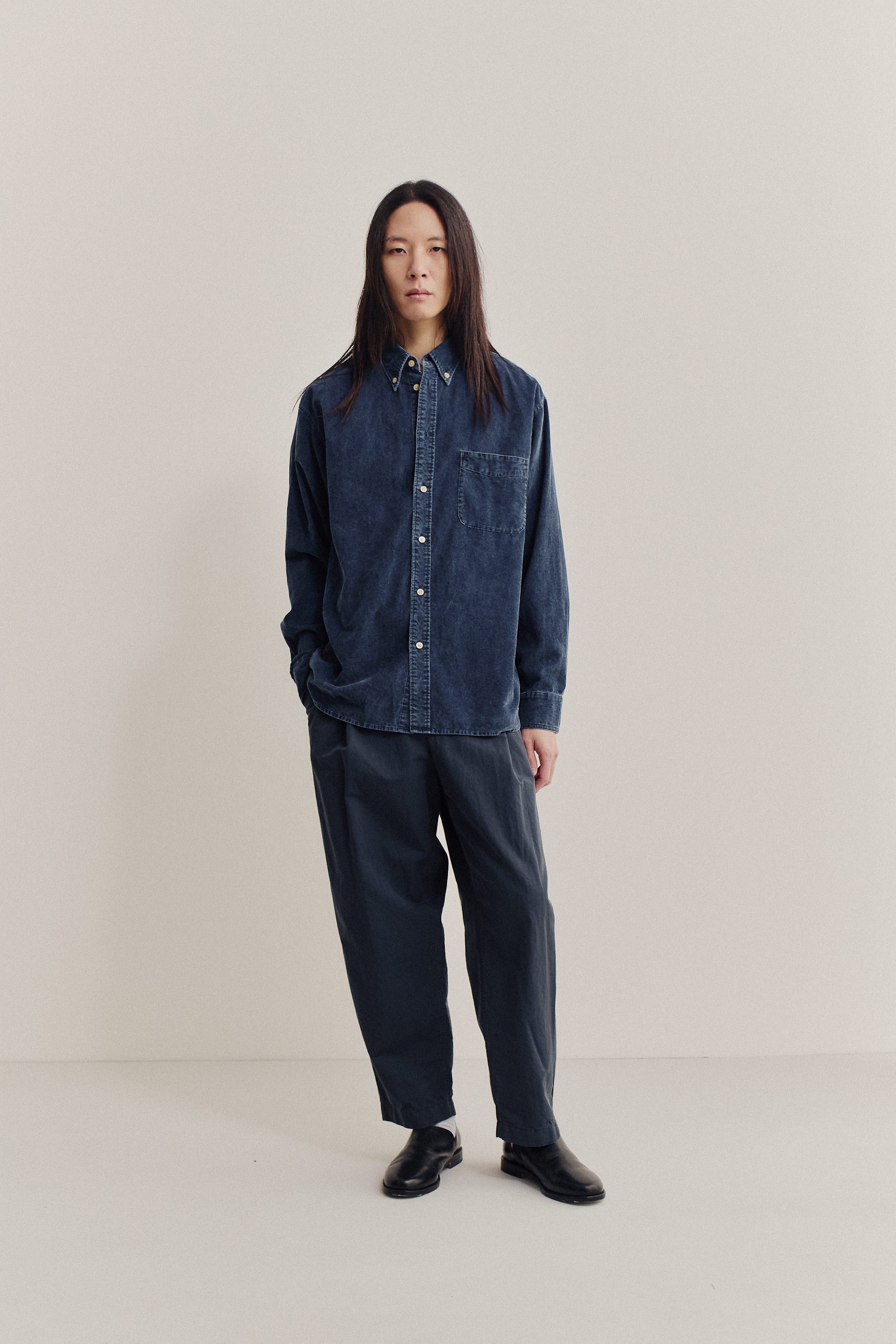 Men's long-sleeved shirt in garment-dyed navy cotton, paired with dark grey cotton-linen trousers.