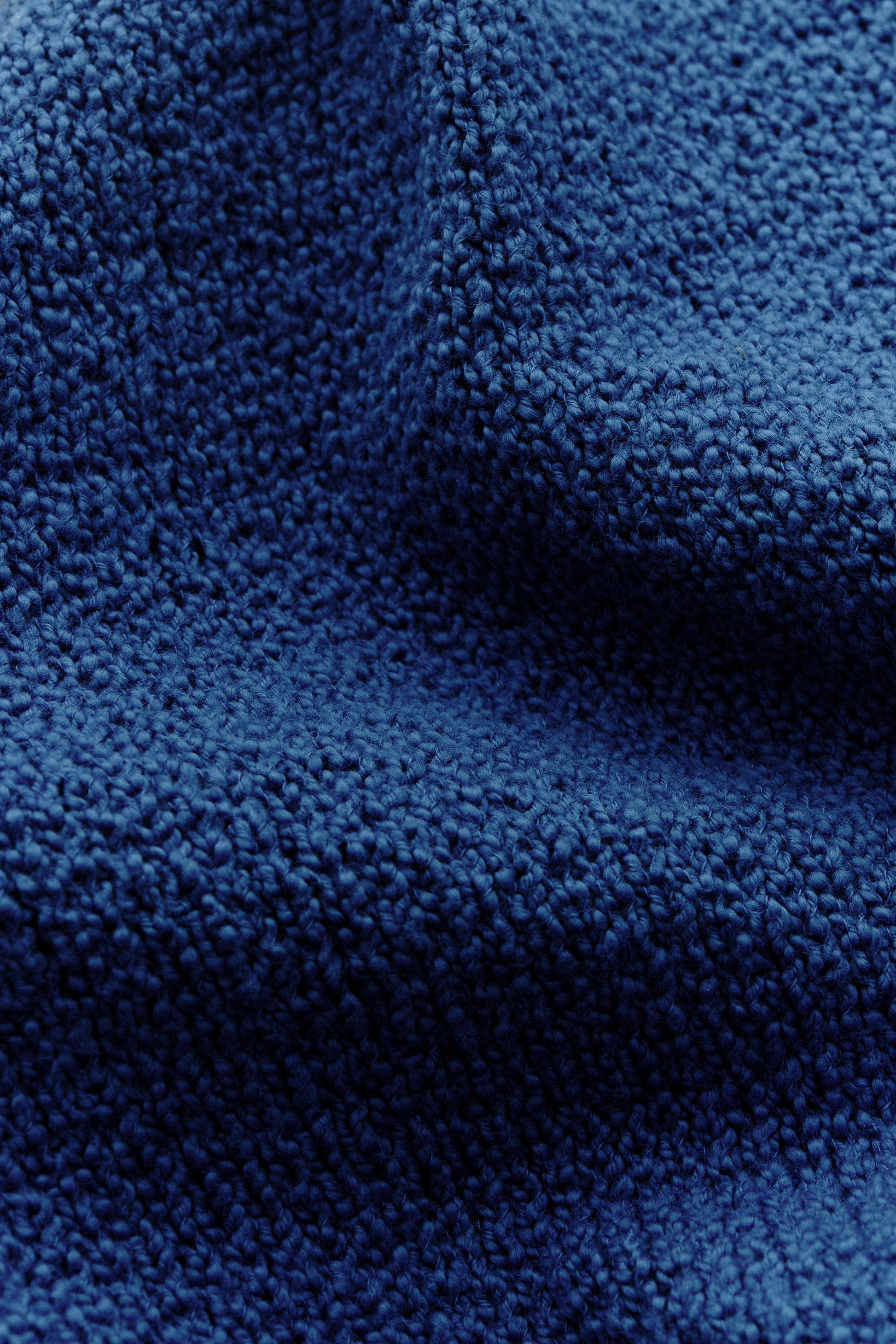 Men's knit polo, organic cotton bouclé, navy blue, close-up of tactile fabric surface.