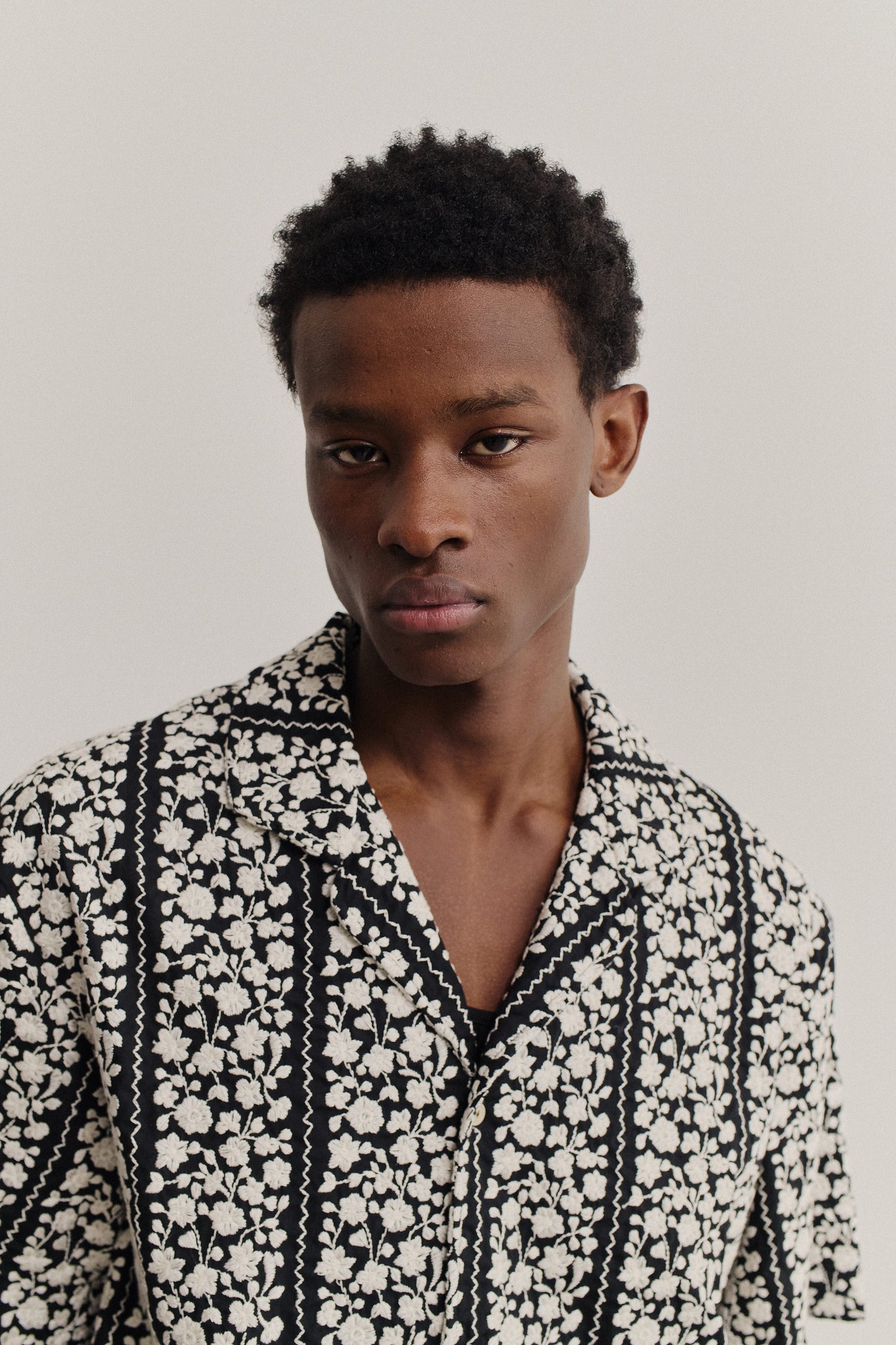 Men's short-sleeved shirt, black 100% cotton with white embroidered floral blocks and wavy lines.