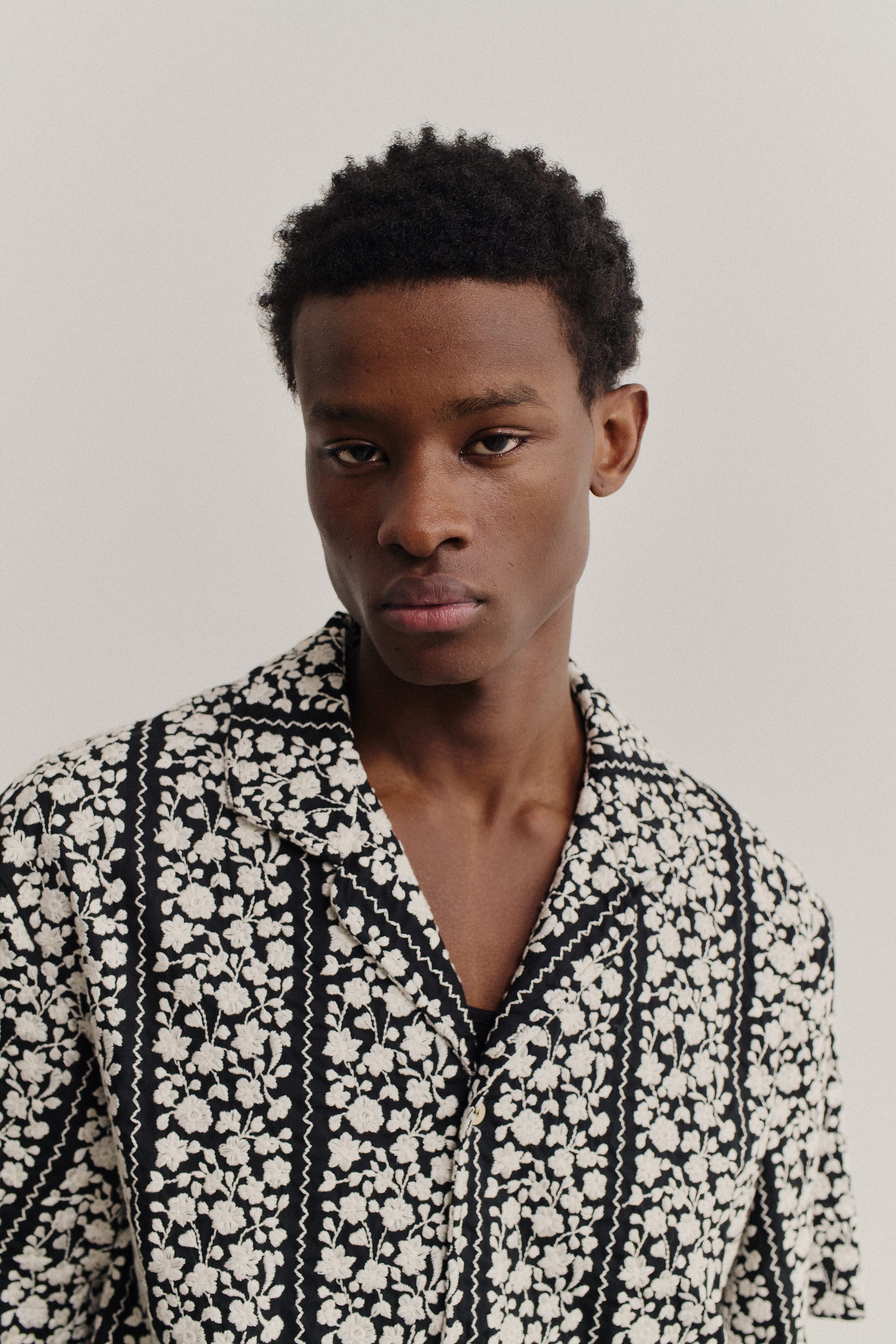 Men's short-sleeved shirt, black 100% cotton with white embroidered floral blocks and wavy lines.