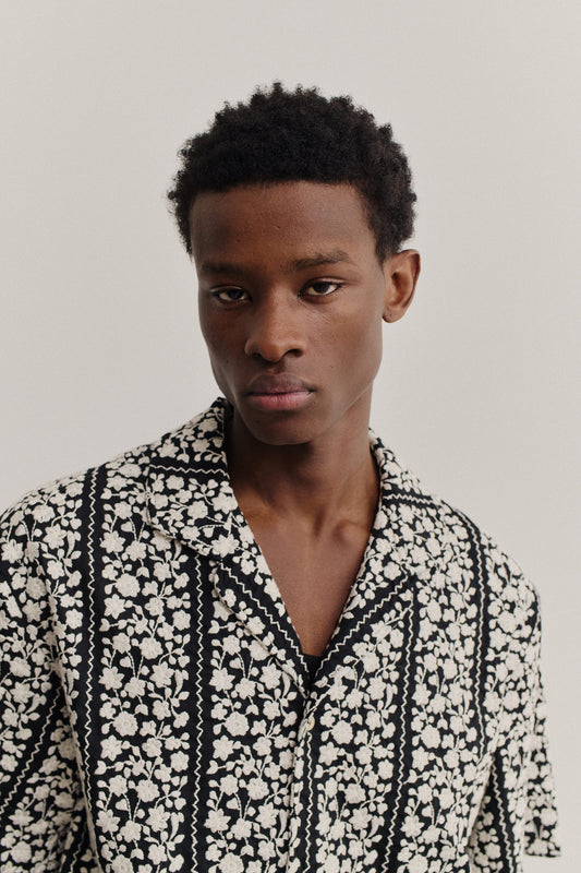 Men's short-sleeved shirt, black 100% cotton with white embroidered floral blocks and wavy lines.