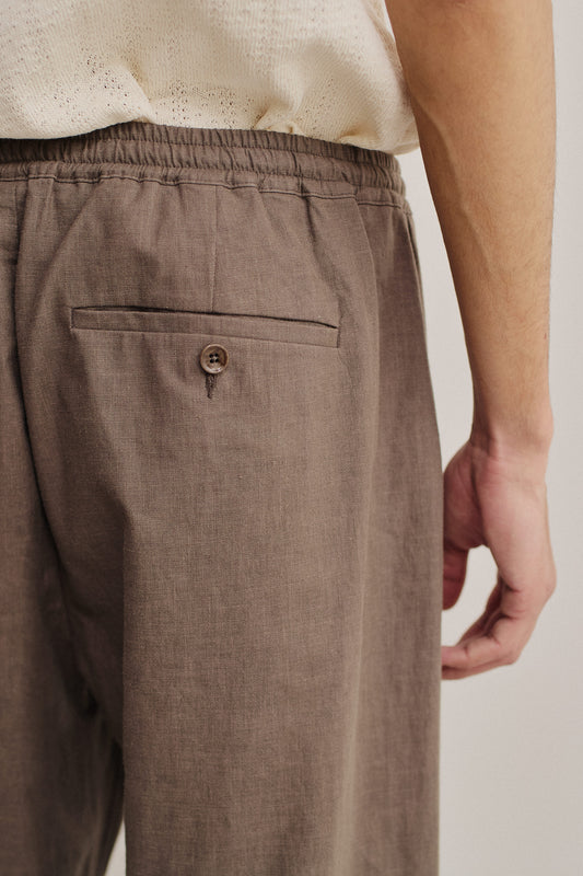 Men's long-pants, 100% linen, natural brown, with elasticated waistband and buttoned welt back pocket.