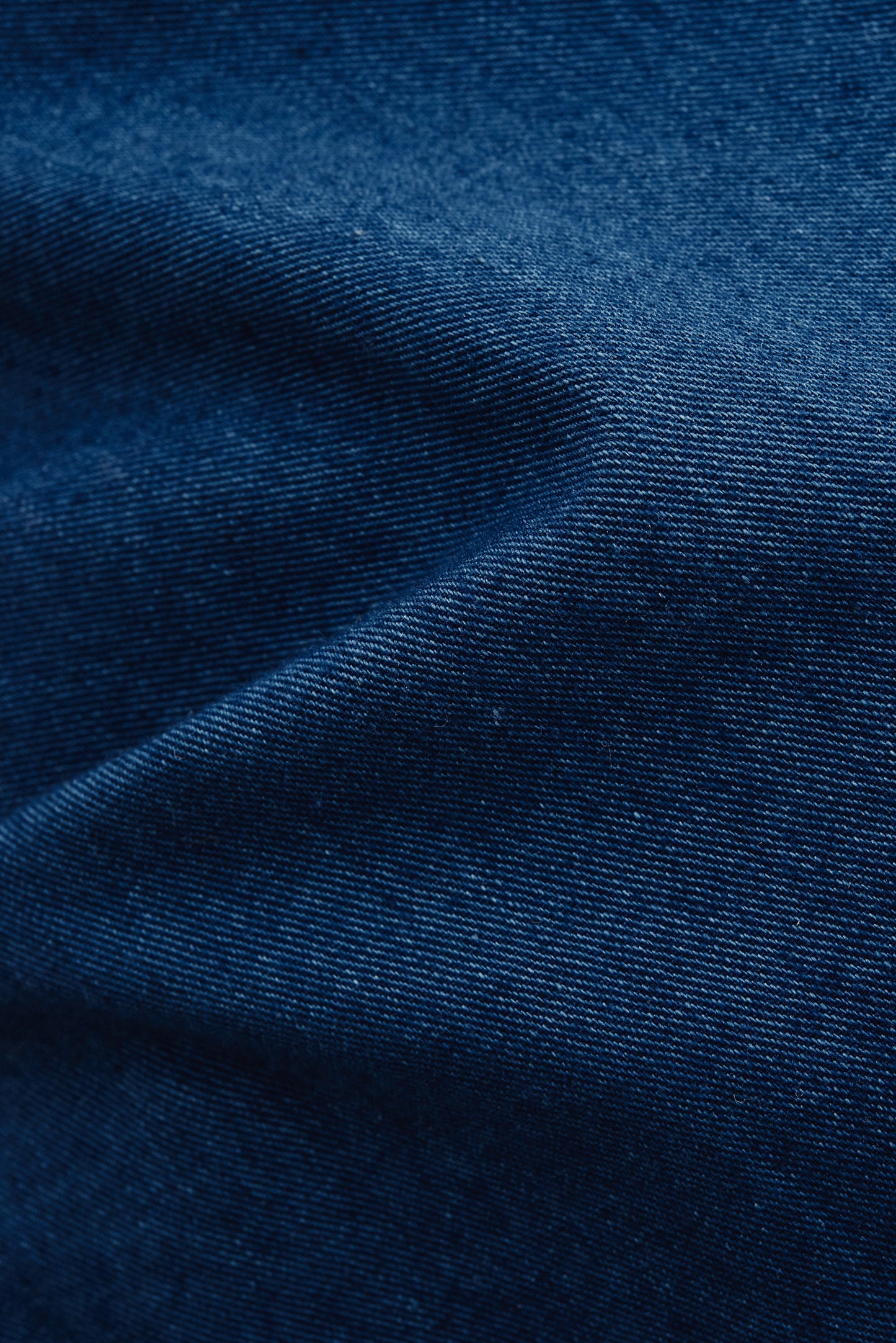 Women's jumpsuit, 100% cotton, washed indigo blue, plain weave fabric with subtle folds.