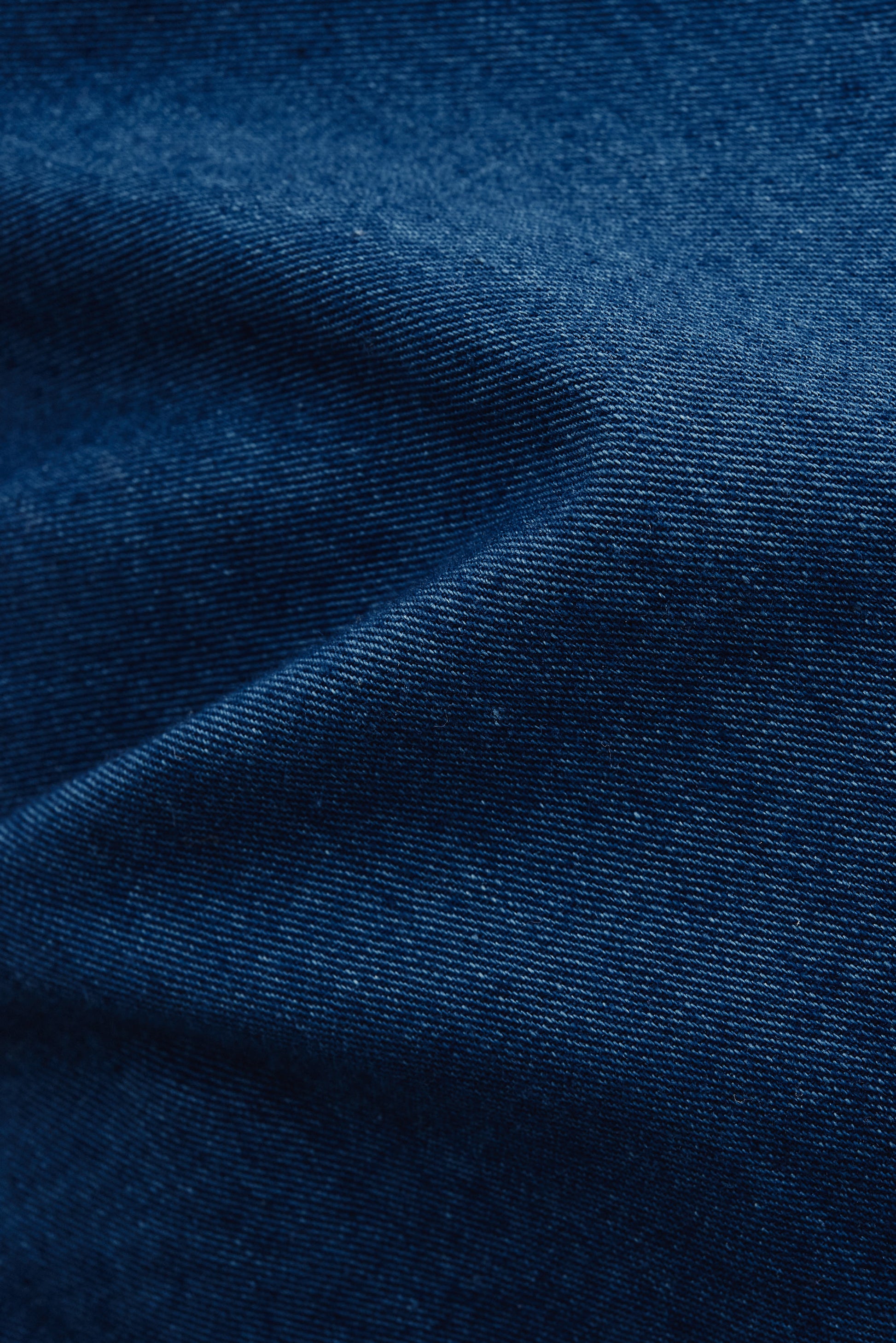 Women's jumpsuit, 100% cotton, washed indigo blue, plain weave fabric with subtle folds.