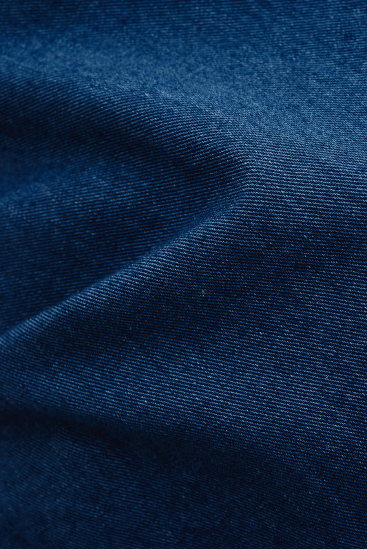 Women's jumpsuit, 100% cotton, washed indigo blue, plain weave fabric with subtle folds.