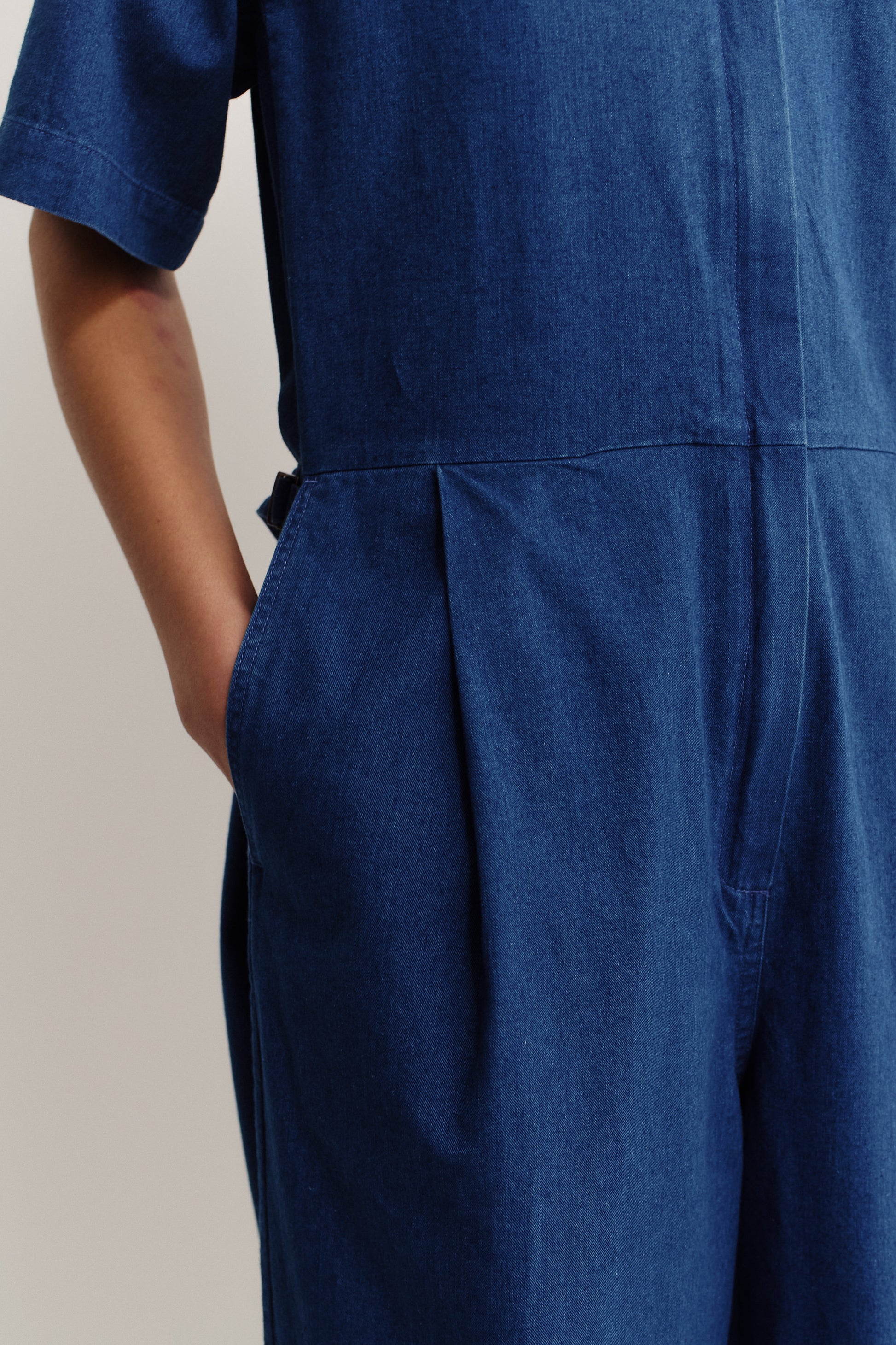 Women's jumpsuit, short-sleeved, wide-leg, washed indigo cotton, with pleats and side pockets.