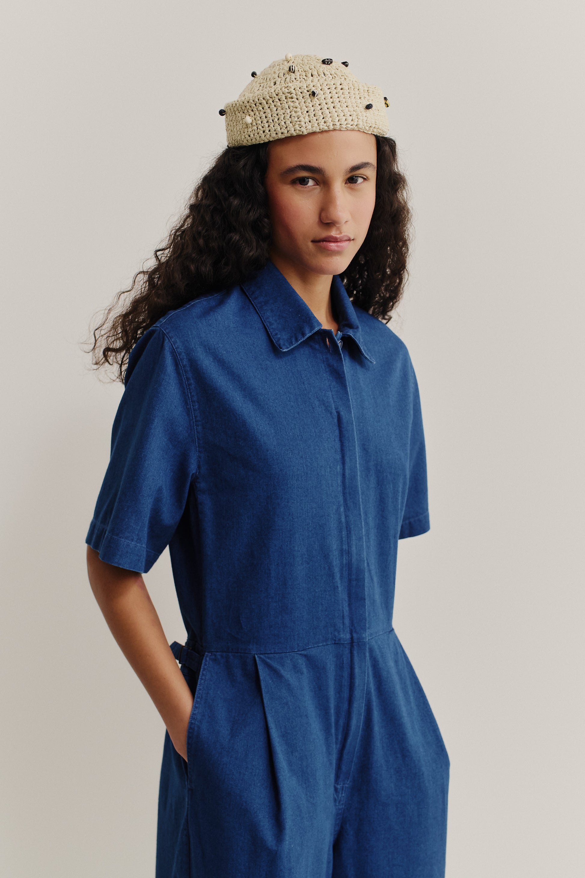 Women's short-sleeved jumpsuit in washed indigo cotton with lay-down collar and front pleats.