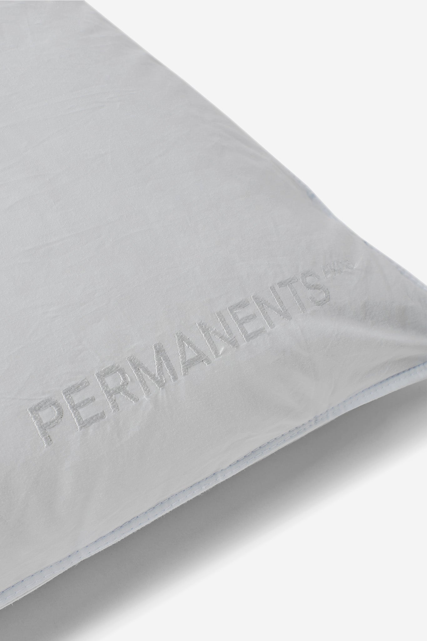 White eiderdown pillow with "PERMANENTS" embroidered logo, soft fabric, and light blue stitching.