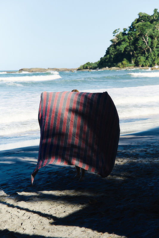 Accessories beach towel, red and navy striped linen-cotton blend, on a sunny beach.